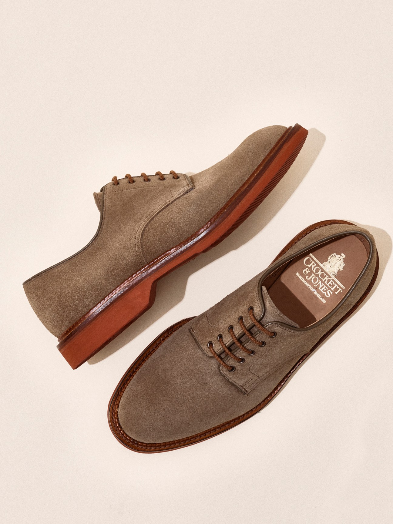 Two brown suede oxford shoes by Crockett & Jones photographed against beige background