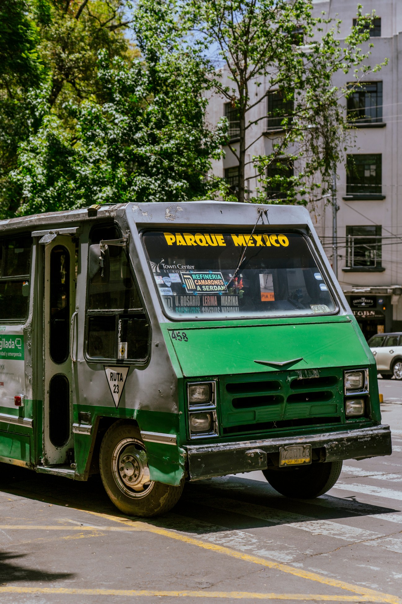 Green and white public bus with Parque Mexico destination sign parked on tree-lined street