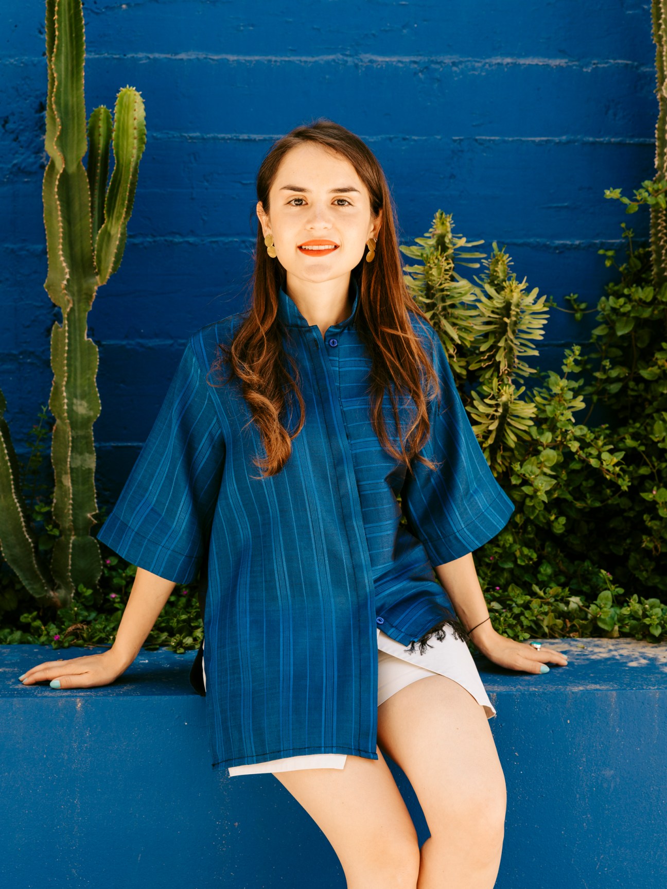 Fashion designer Anissa Meddeb sitting against a blue wall with cacti and plants in the background