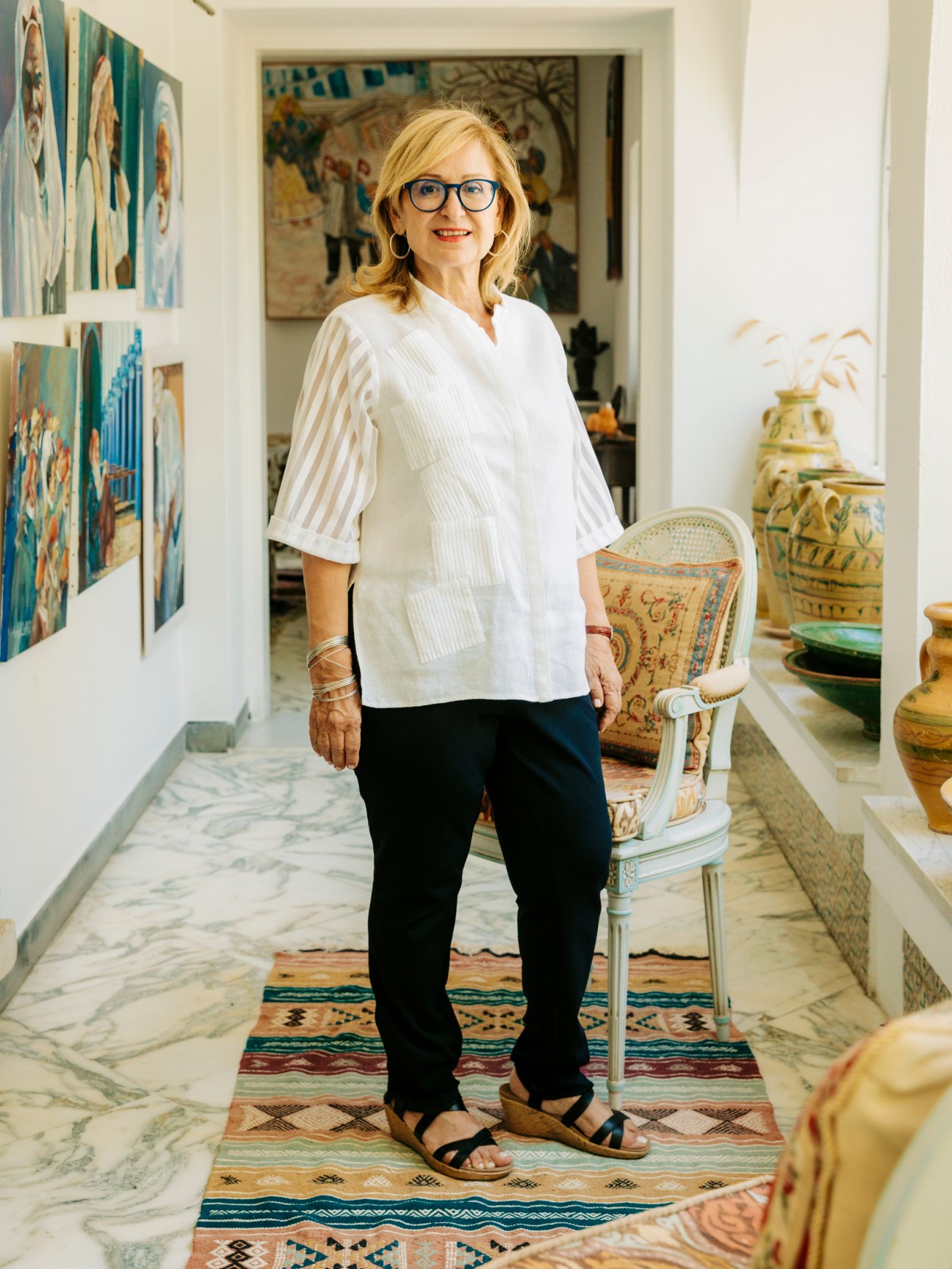 Achraf Bahri Meddeb standing in an art-filled interior space with colorful paintings and decorative objects