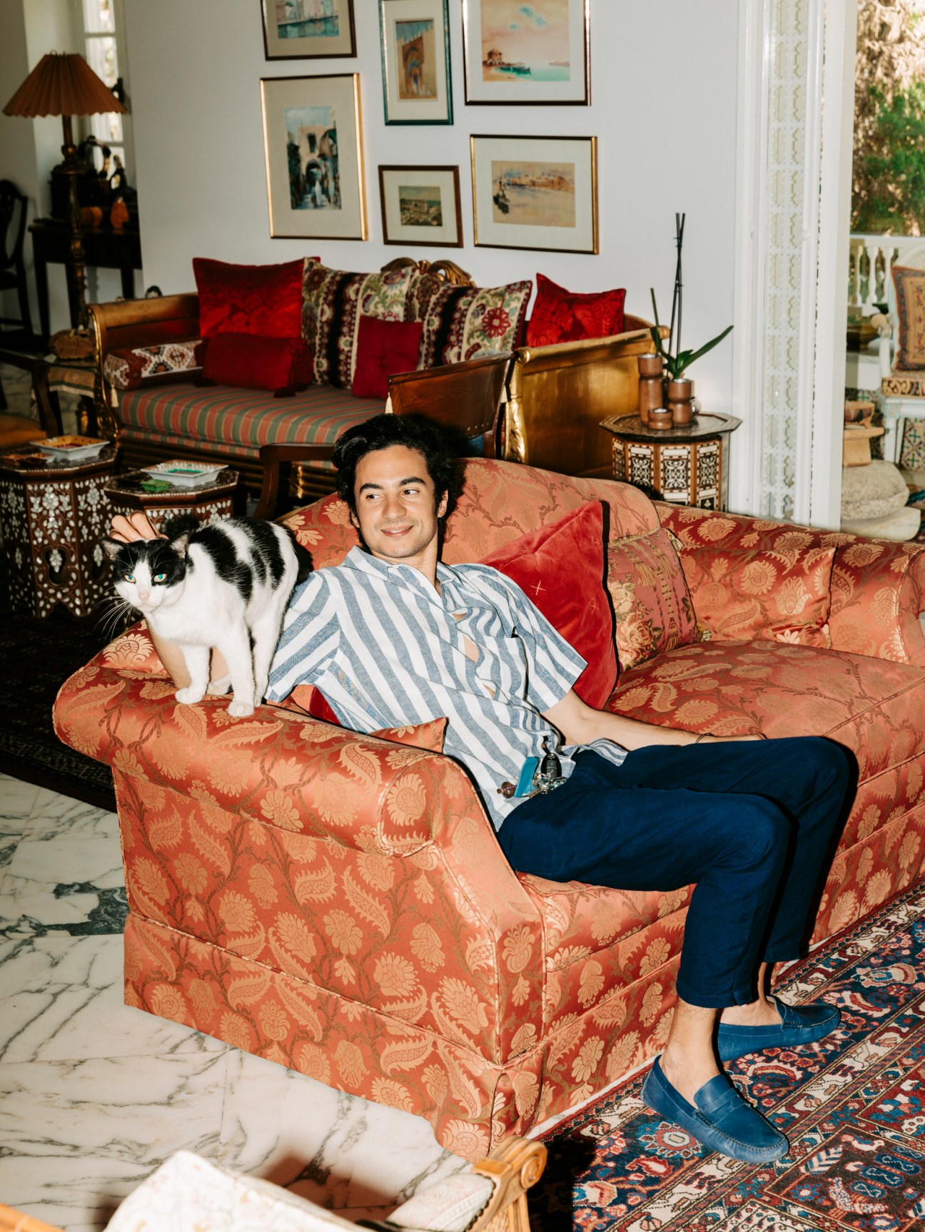 Architect Hassene Jeljeli relaxing in an ornate armchair with a black and white cat in an elegantly furnished living room