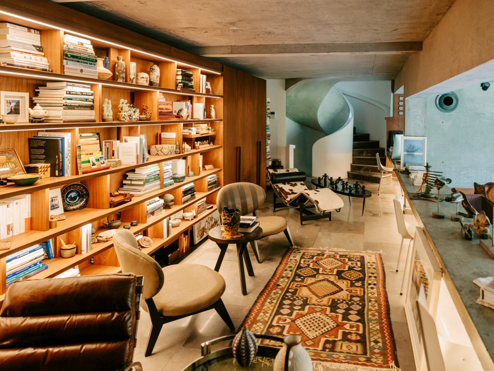 Modern interior with wooden built-in bookshelves, mid-century chairs, patterned rug and curved staircase