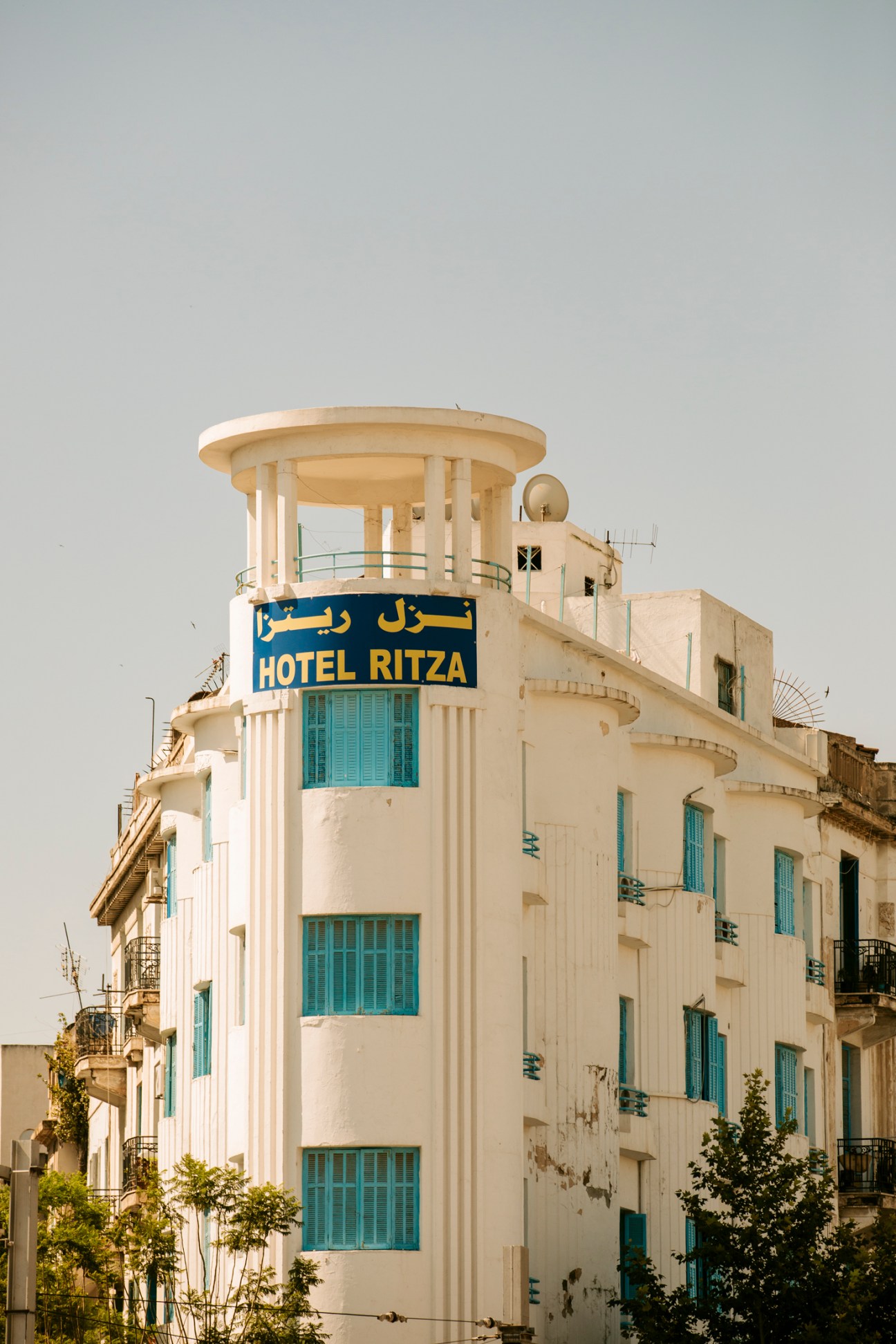 White modernist Hotel Ritza building with cylindrical tower, blue shutters and Arabic signage in Tunis