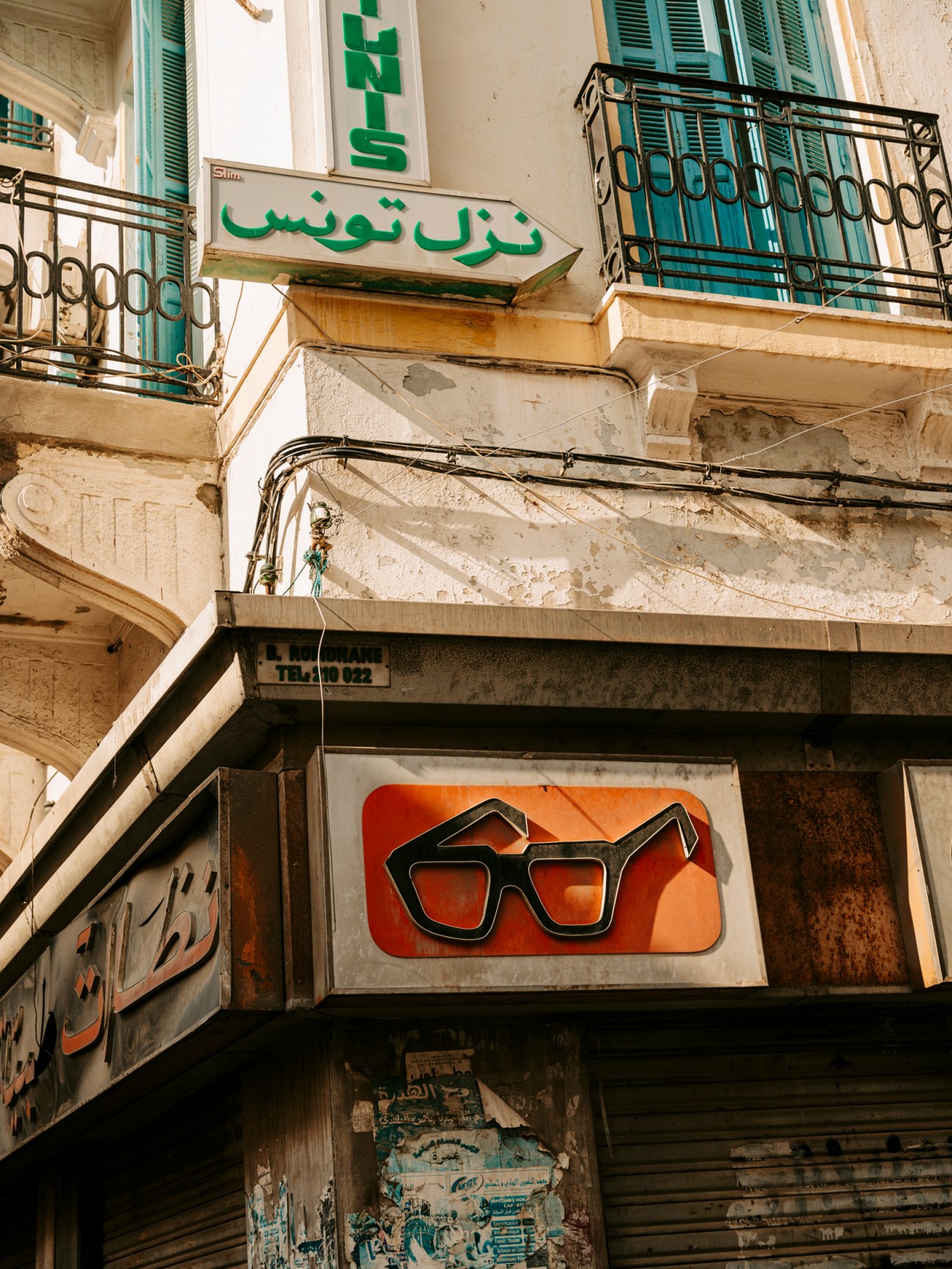 Vintage Arabic and French signage on weathered building facade with ornate balcony railings in central Tunis