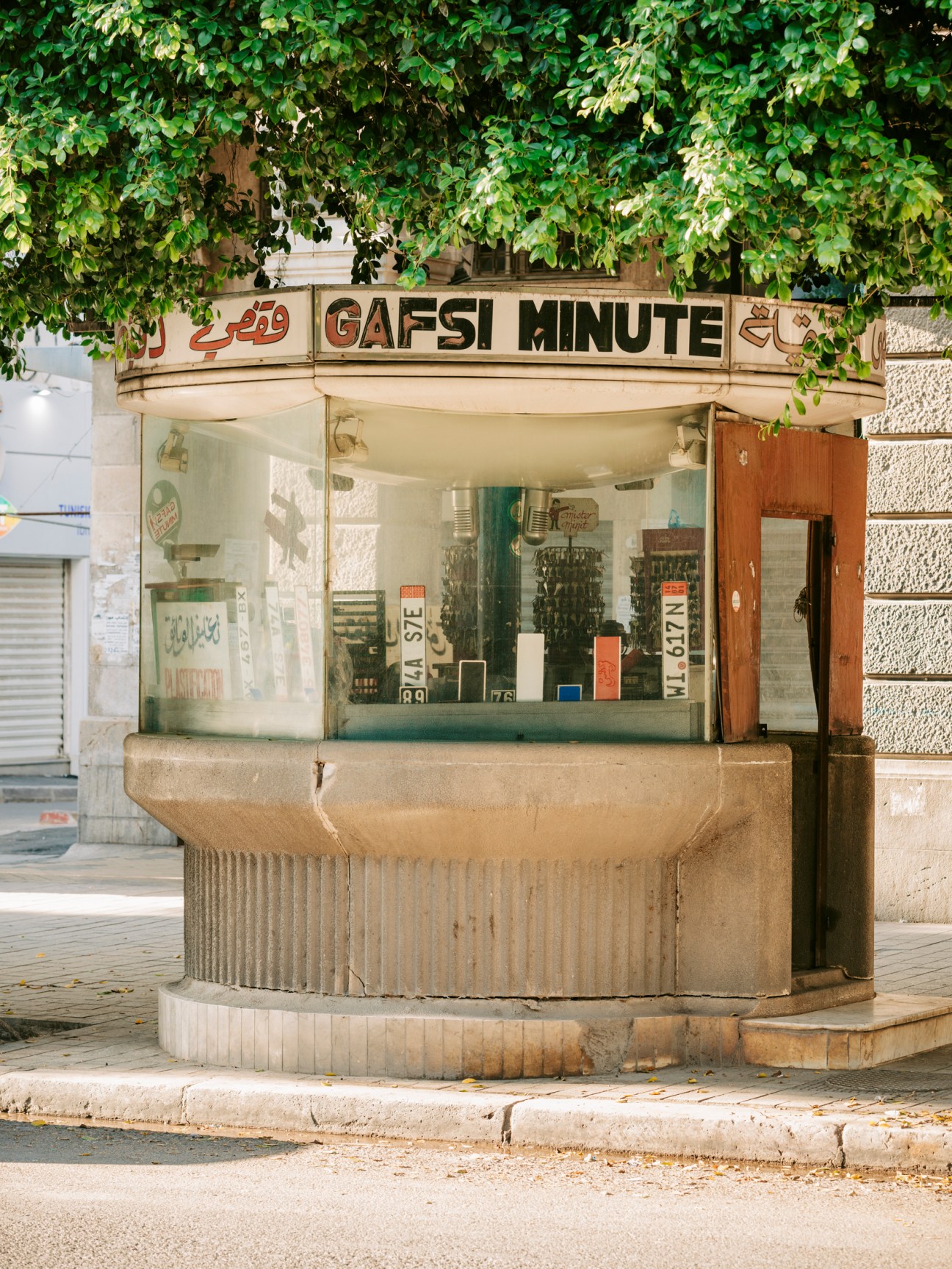 Small street kiosk with glass display case labeled 'GAFSI MINUTE' selling various items