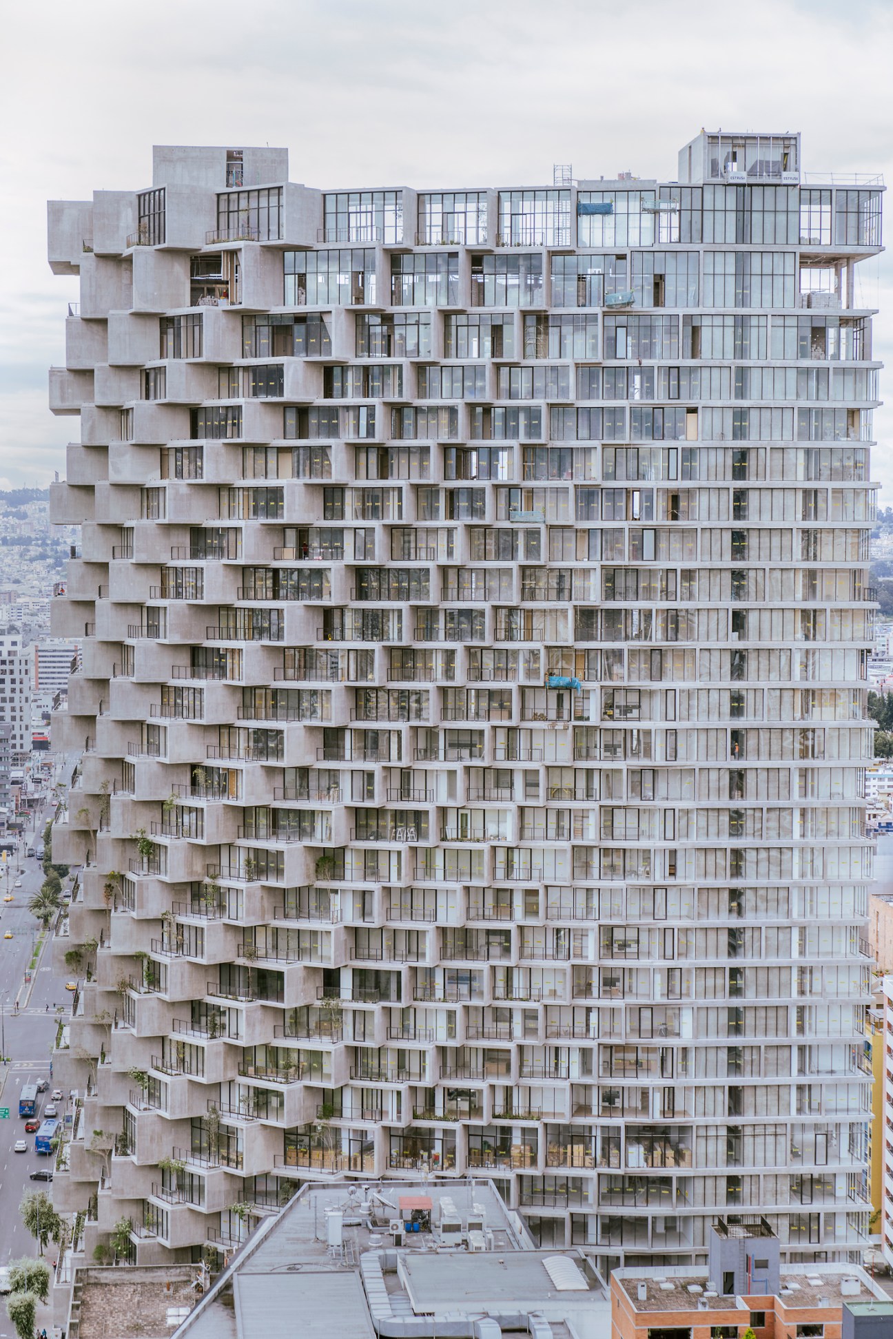 Tall modern concrete residential tower with protruding balconies against cloudy sky in urban setting
