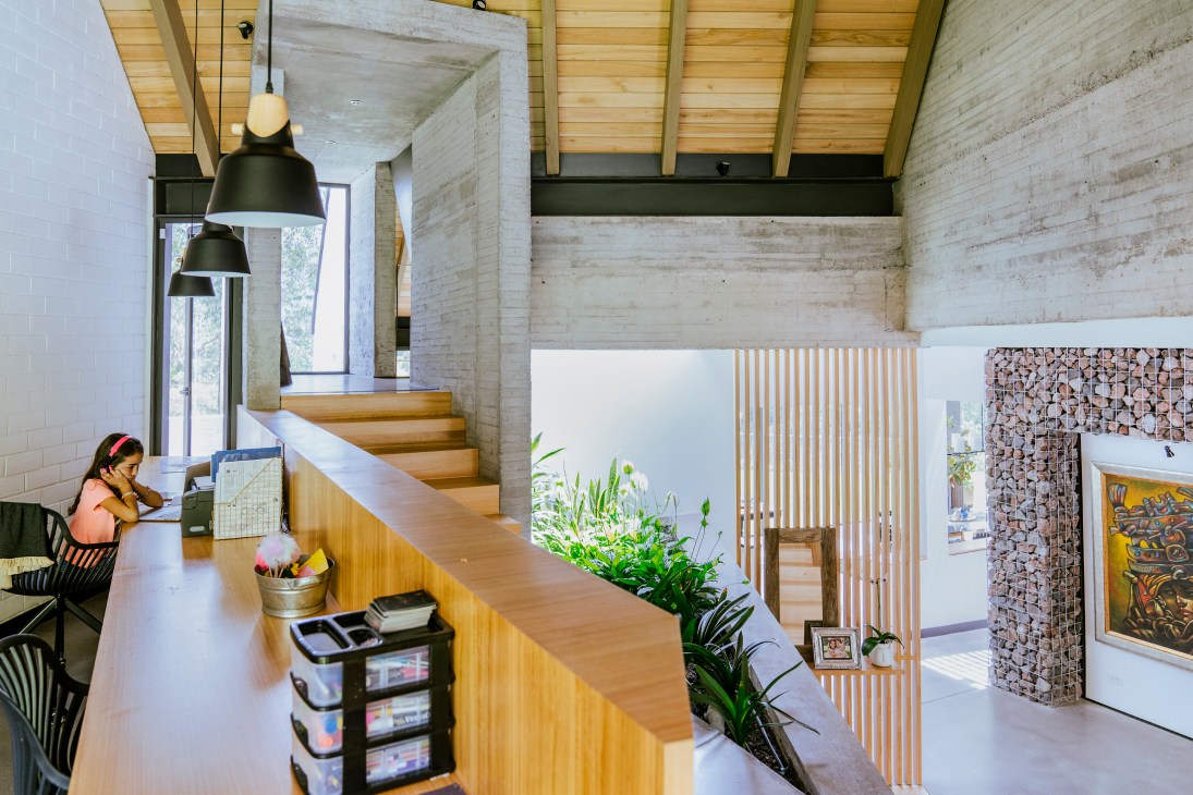 Modern interior with exposed concrete ceiling, wooden beams, kitchen island, and person working at desk