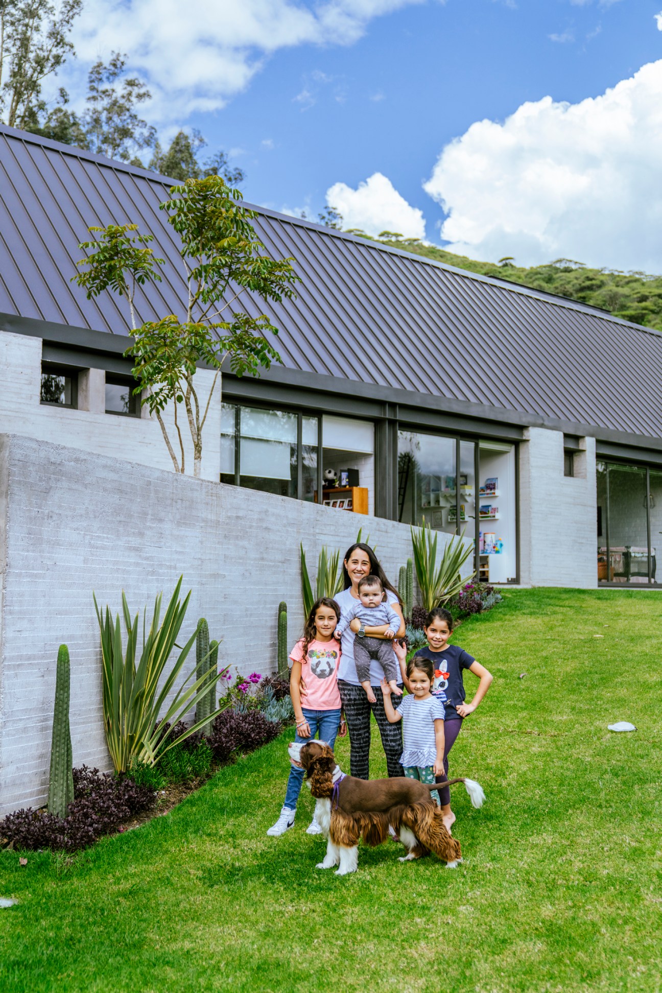 Family with children and dog posing outside modern white house with metal roof designed by Diez + Muller