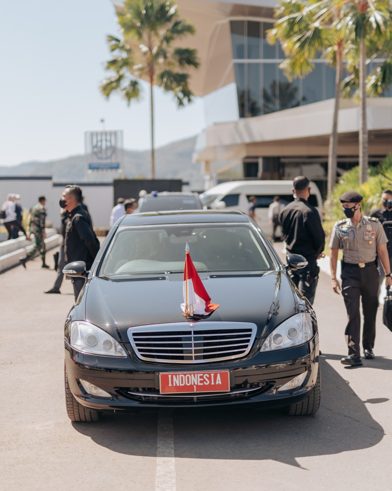 Black Mercedes-Benz sedan with Indonesian flag and INDONESIA license plate surrounded by uniformed security personnel