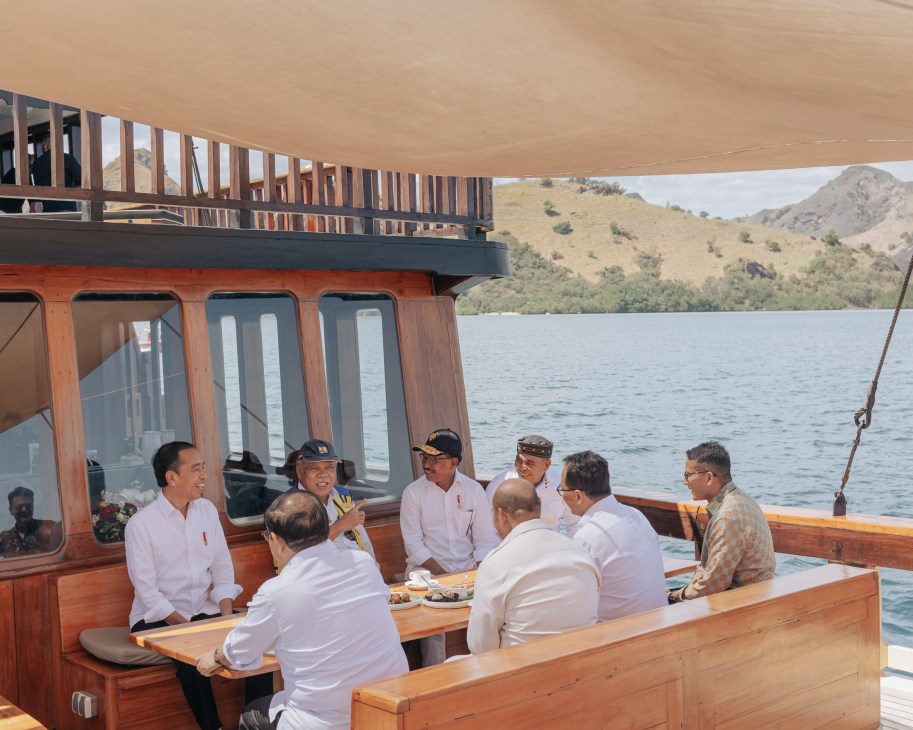 Indonesian President Joko Widodo meets with cabinet members on wooden boat deck with mountainous coastline in background