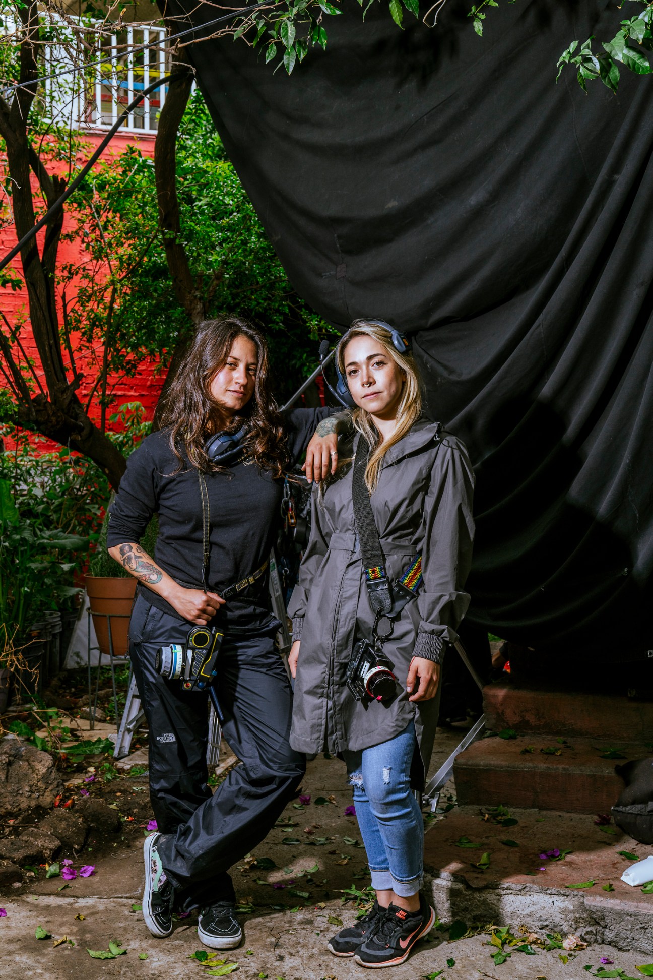 Two women with film equipment and cameras standing outdoors in a garden setting