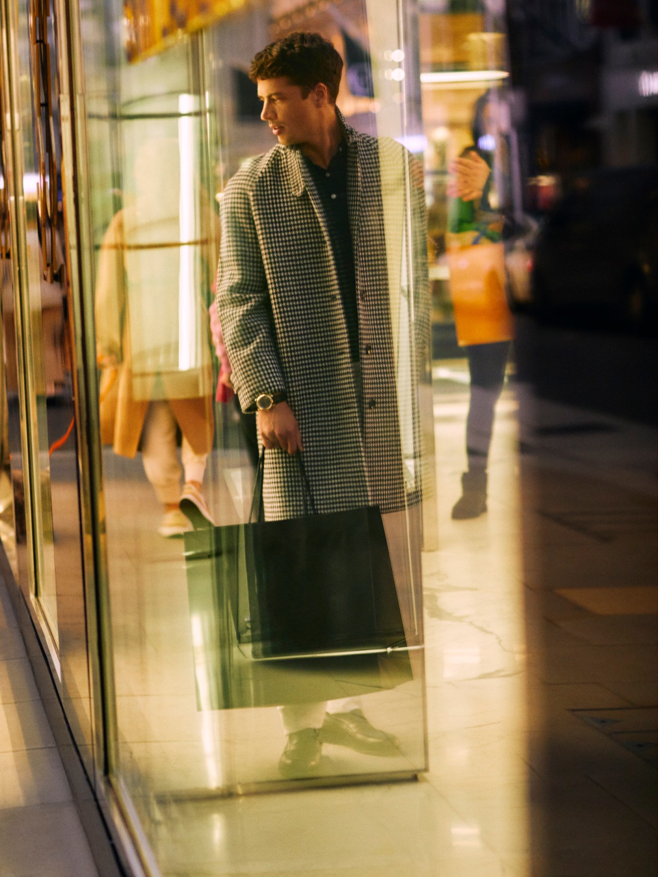 Man in houndstooth coat and navy polo shirt checking his watch while window shopping