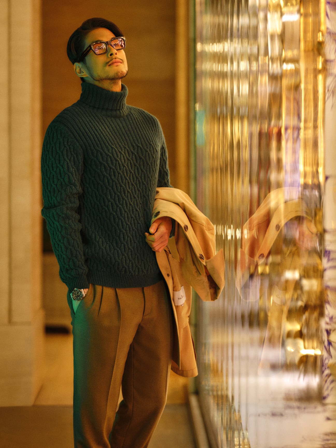 Man in coat and rollneck jumper wearing glasses and checking his watch
