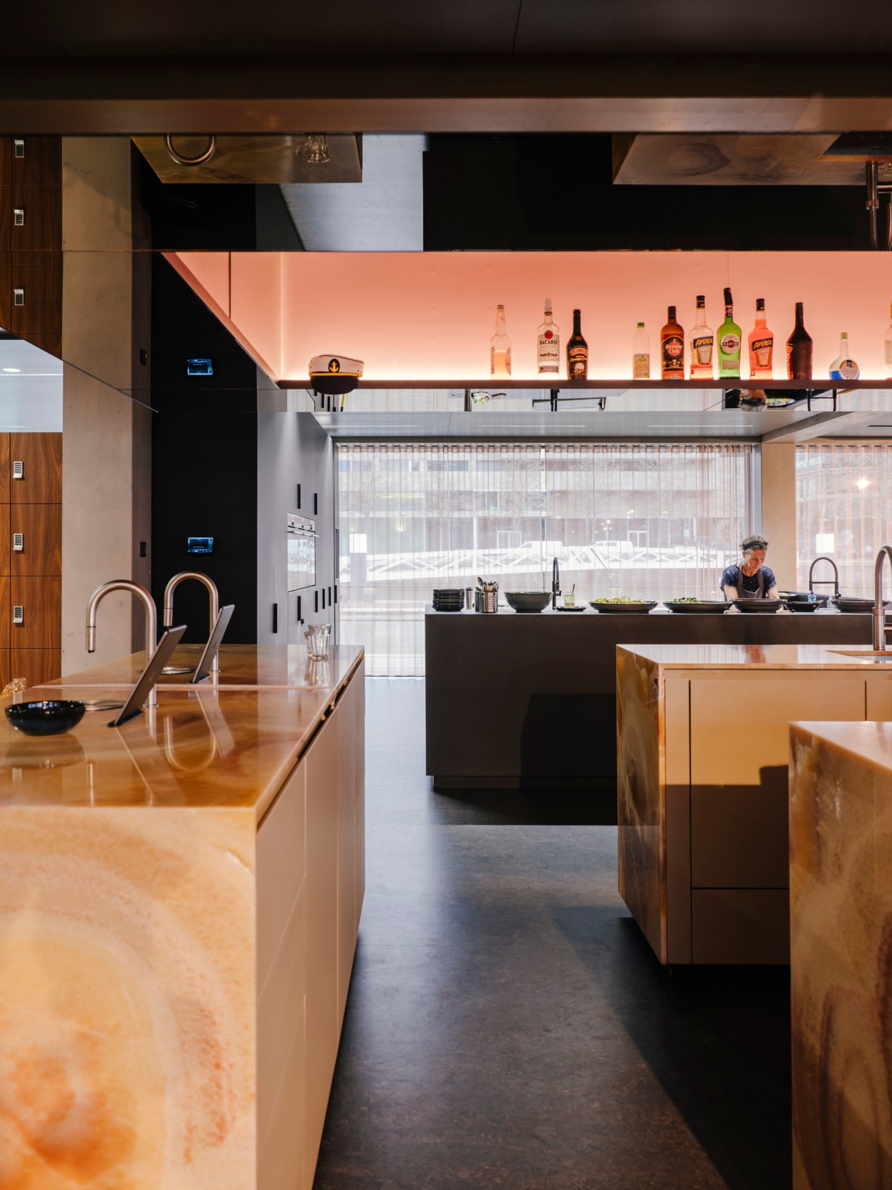 Modern kitchen interior with warm wood cabinets, stone countertops, and backlit bar area with bottles