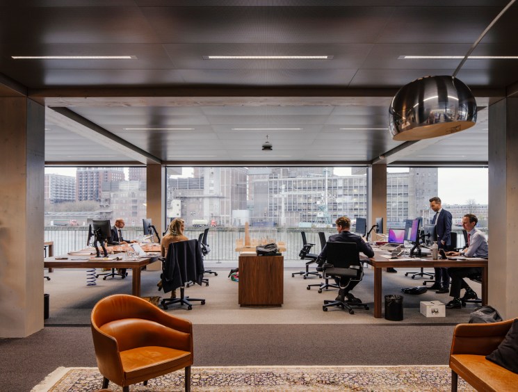 Modern open-plan office interior with exposed timber beams, floor-to-ceiling windows, and city skyline views