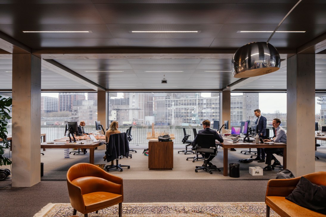 Modern open-plan office interior with exposed timber beams, floor-to-ceiling windows, and city skyline views