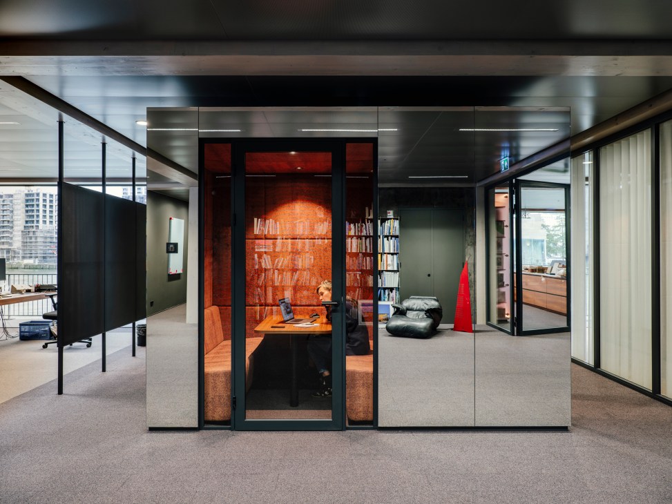 Interior workspace with orange-lit glass-walled pod, exposed timber ceiling, and modern office furniture