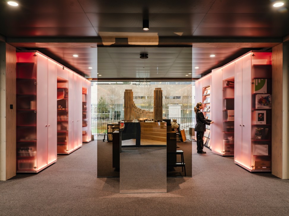Interior library or reading area with illuminated display cases, wooden furniture and person browsing materials