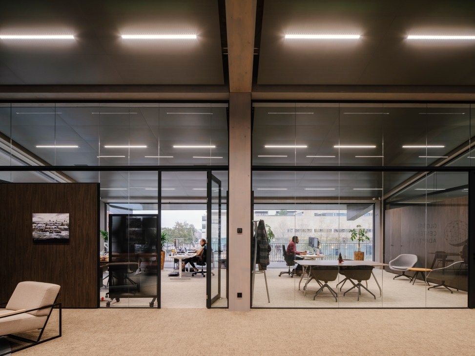 Glass-walled meeting rooms and offices showing timber frame construction with harbour views beyond