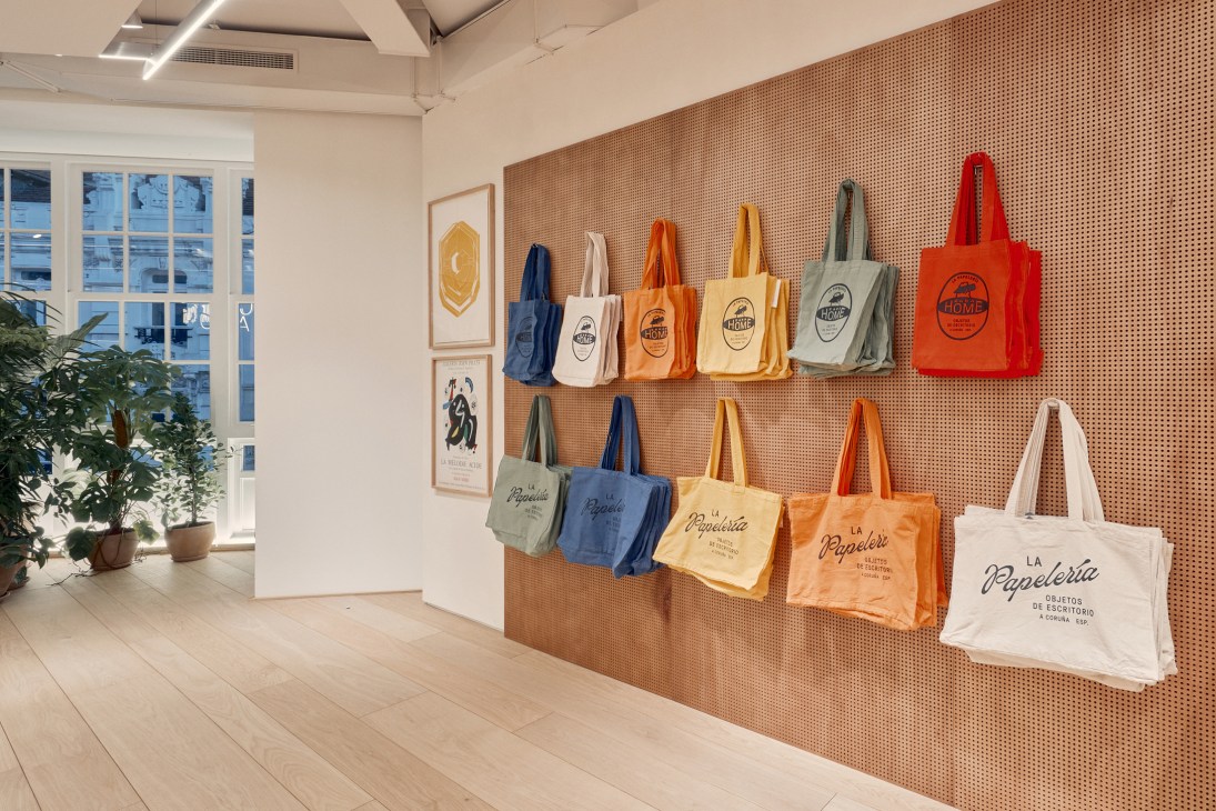 Colorful cotton tote bags with La Papelería branding displayed on pegboard wall in retail store