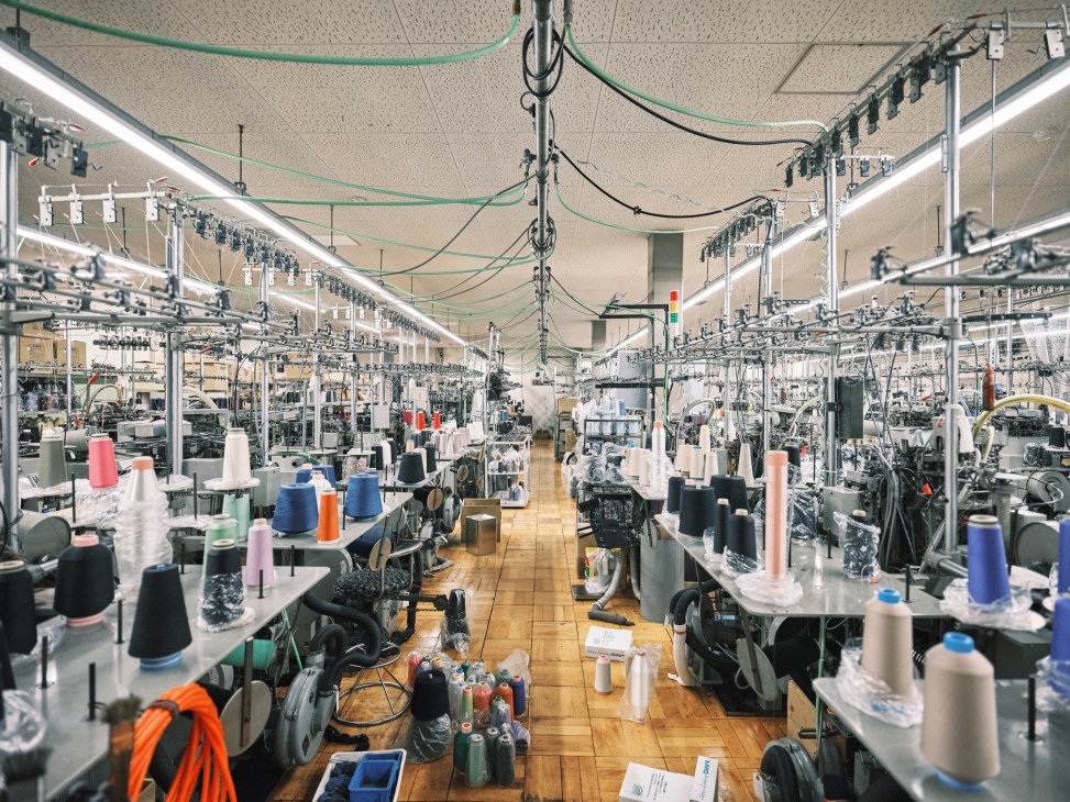 Interior view of textile factory showing knitting machines, colorful thread spools, and manufacturing equipment