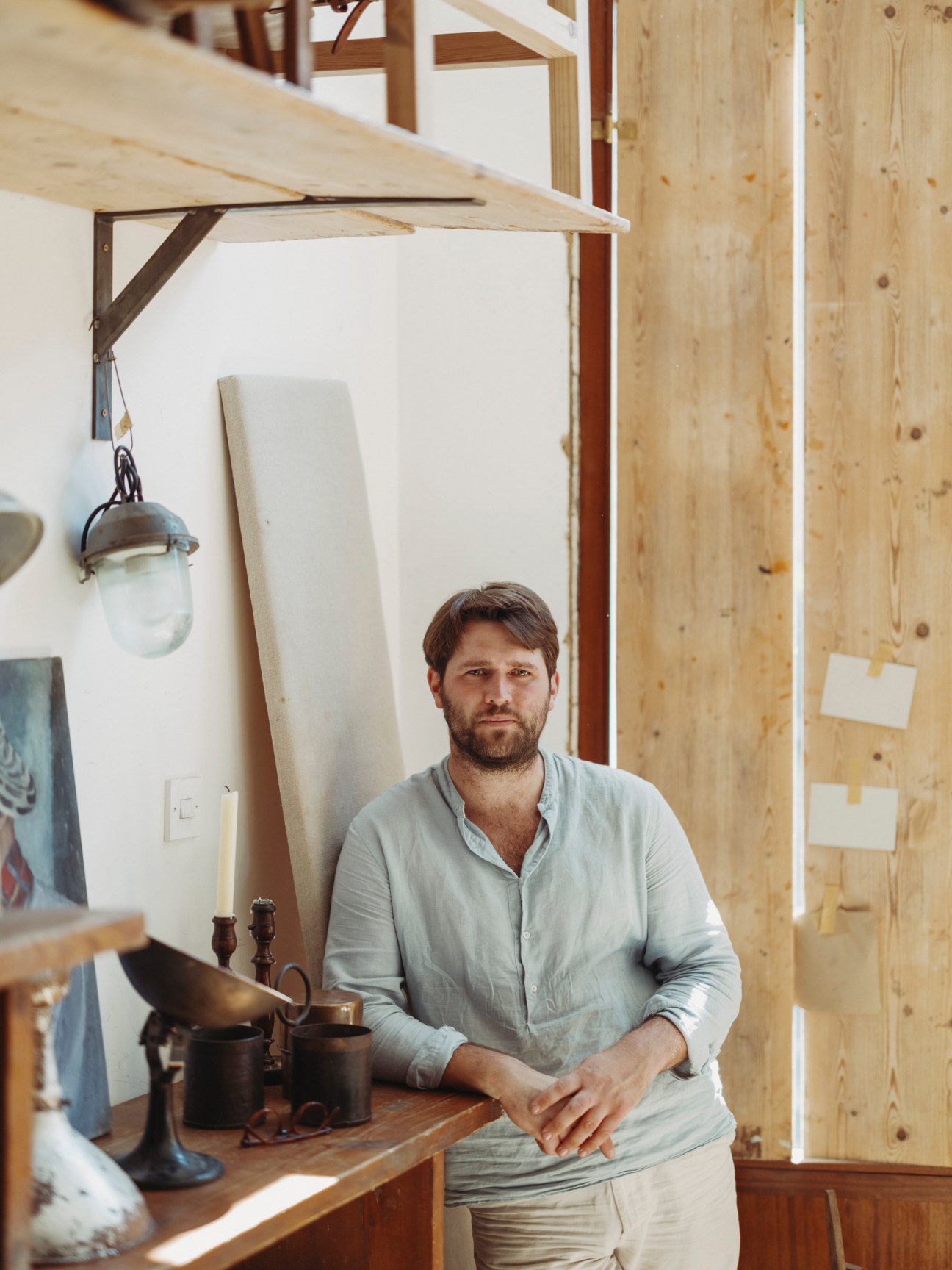 Man in light blue shirt standing in wooden workshop with leather crafting tools and materials
