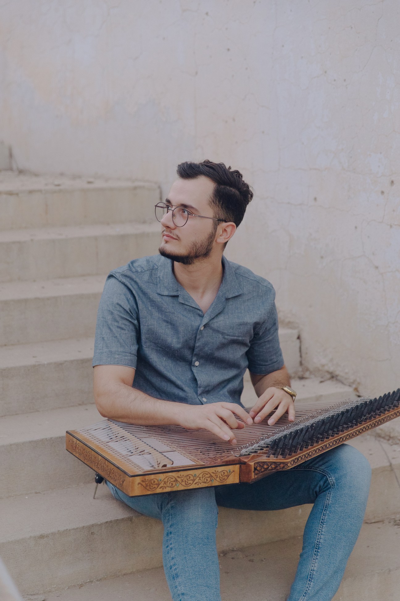 Young man with glasses playing an ornate stringed instrument while sitting on stone steps