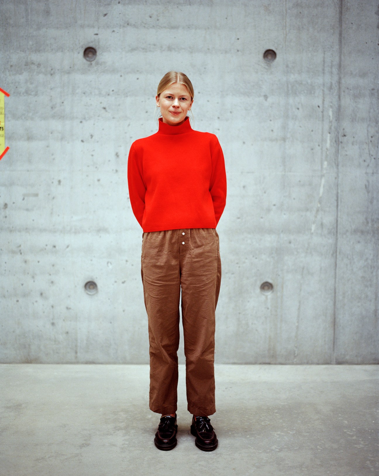 Julie Houborg, a BA architecture student, standing against concrete wall wearing red turtleneck and brown pants