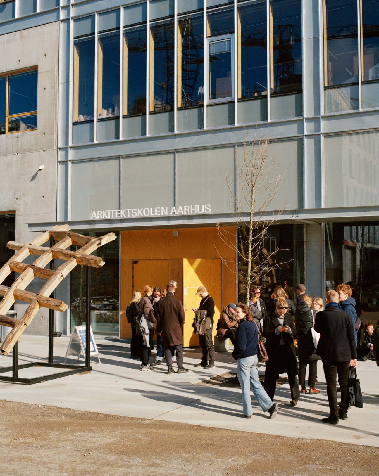 People gathered outside the entrance of Arkitektskolen Aarhus with modern glass and concrete building facade