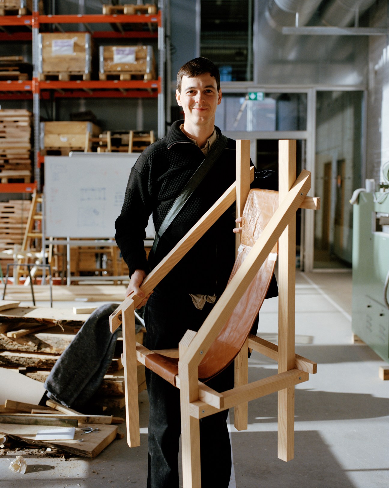 Student Peder Kjærvik holding a wooden chair in a workshop warehouse setting with shelving in background