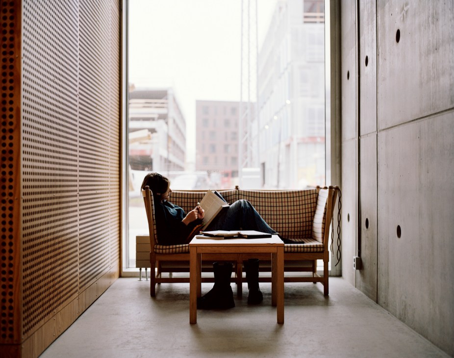 Student reading a book while lying on a bench in a modern interior with concrete walls and perforated screens