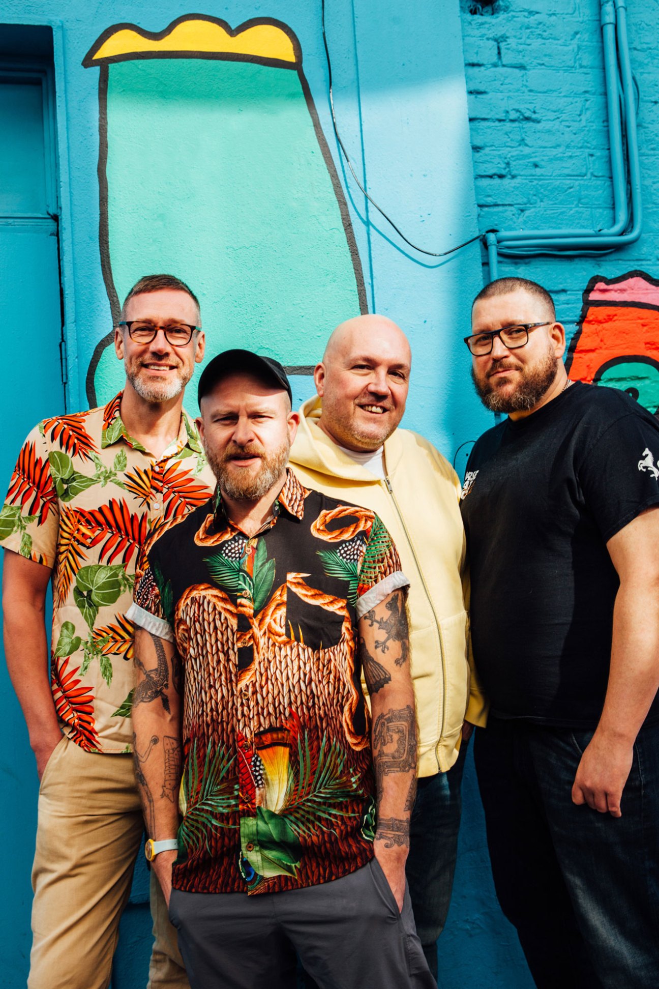 Four men from Horse Meat Disco standing together in colorful shirts against blue graffitied wall
