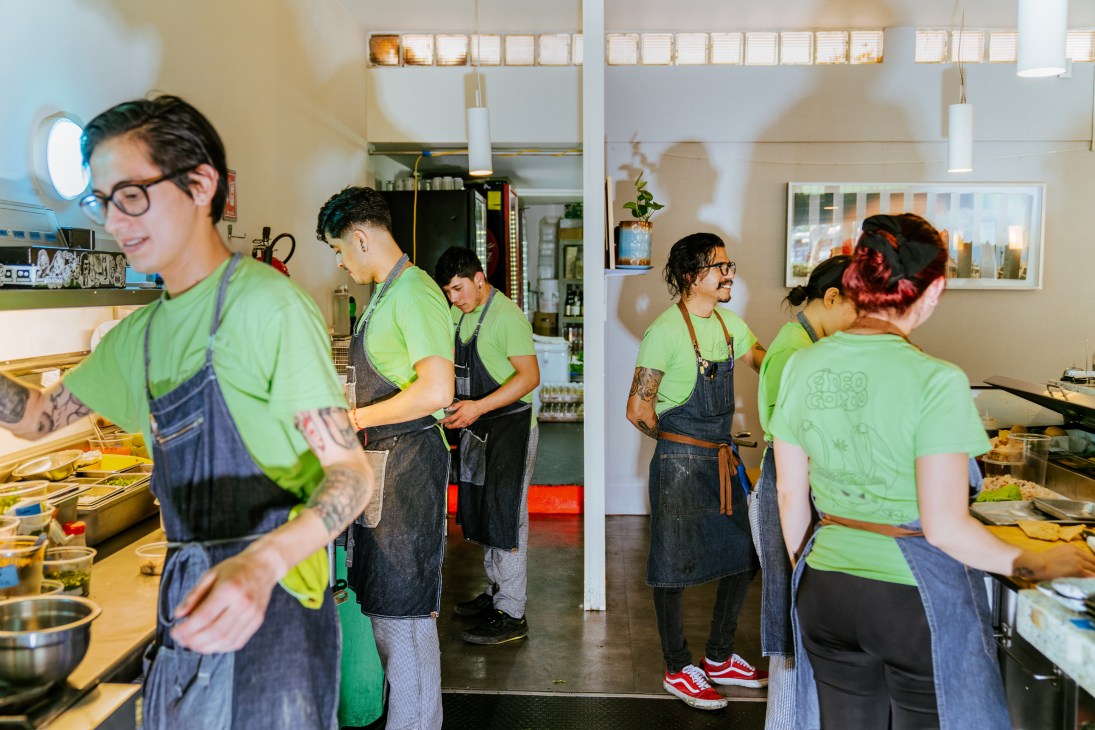 Kitchen staff in bright green t-shirts and dark aprons working in the open kitchen at Fideo Gordo restaurant