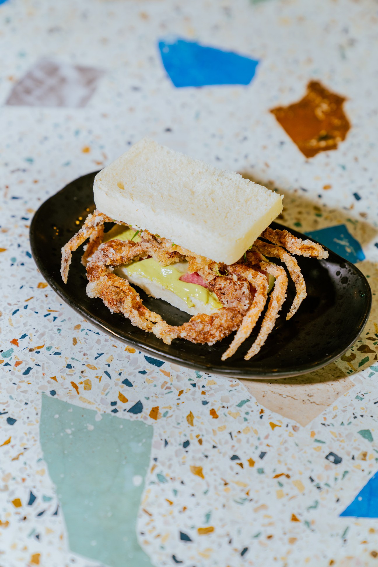 Sliced sandwich with filling on black plate alongside white bread on terrazzo surface at Fideo Gordo