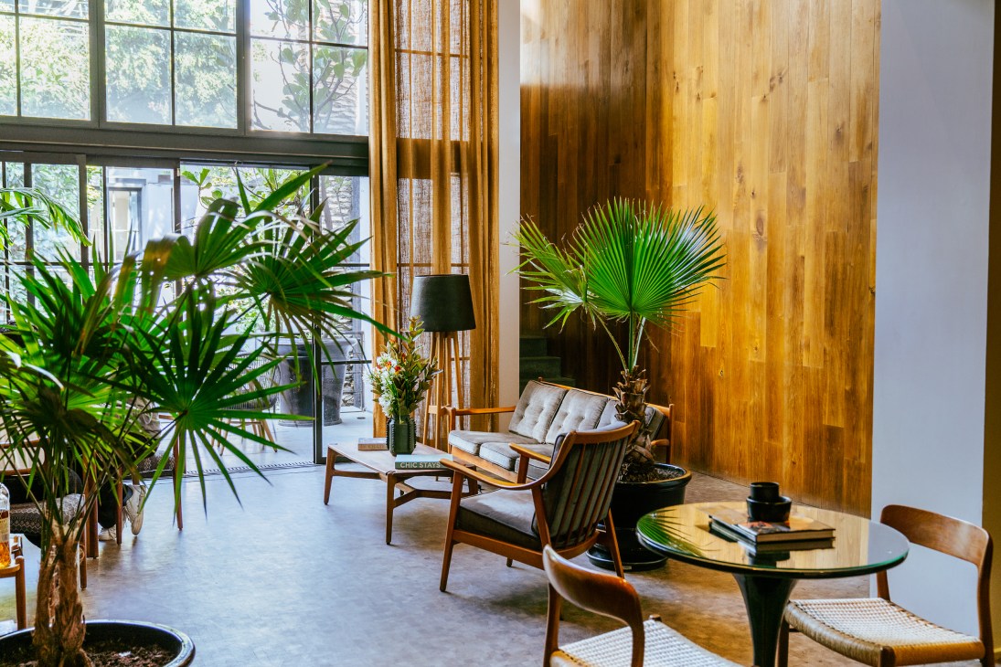 Modern hotel lobby with mid-century furniture, large windows, palm plants, and warm wood paneling