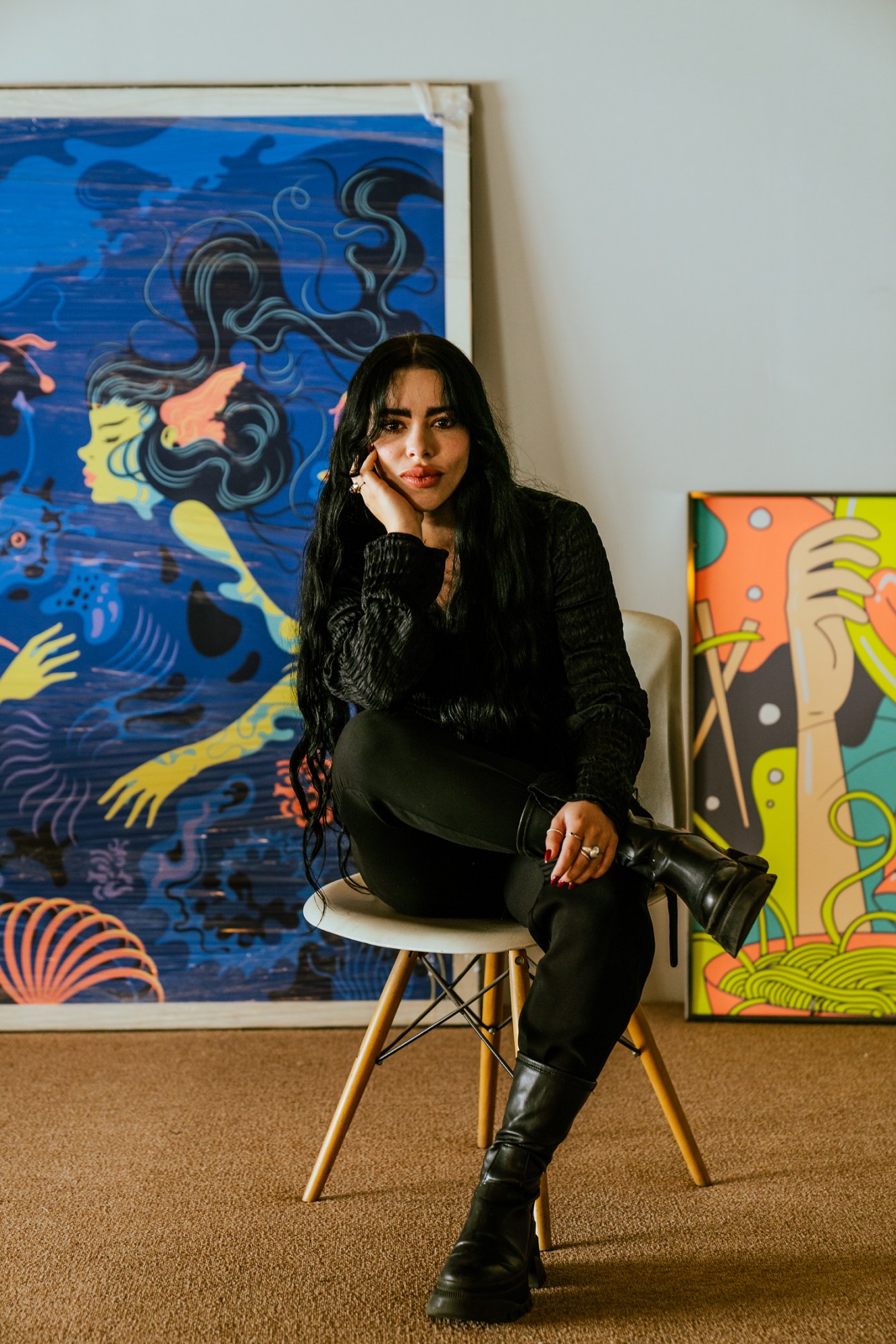 Brenda Urcid sits in a white chair against colorful artwork in her design studio