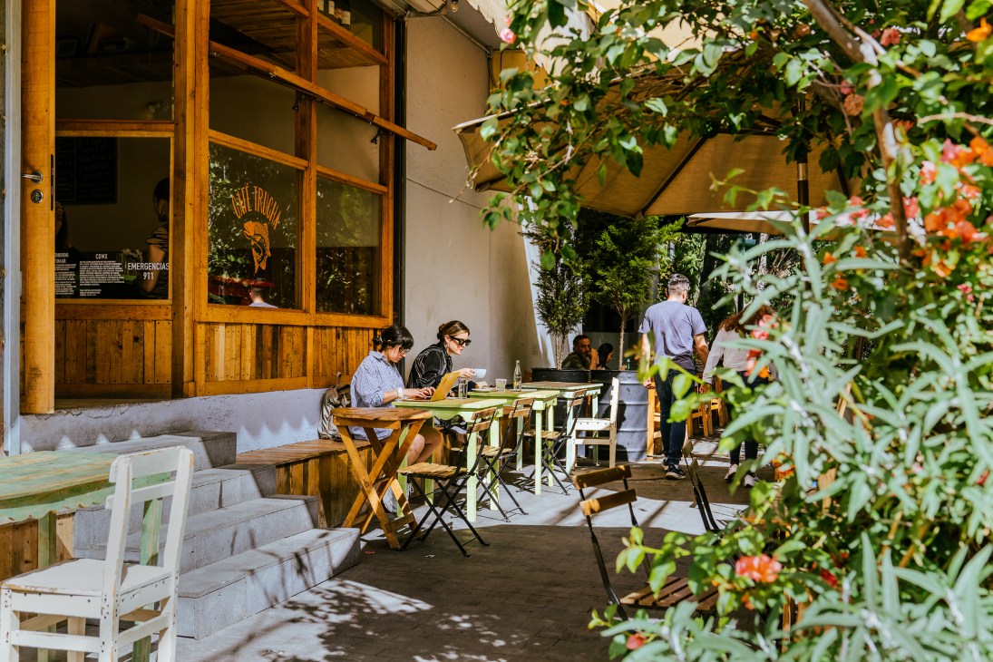 Person sitting at outdoor cafe table working on laptop with coffee