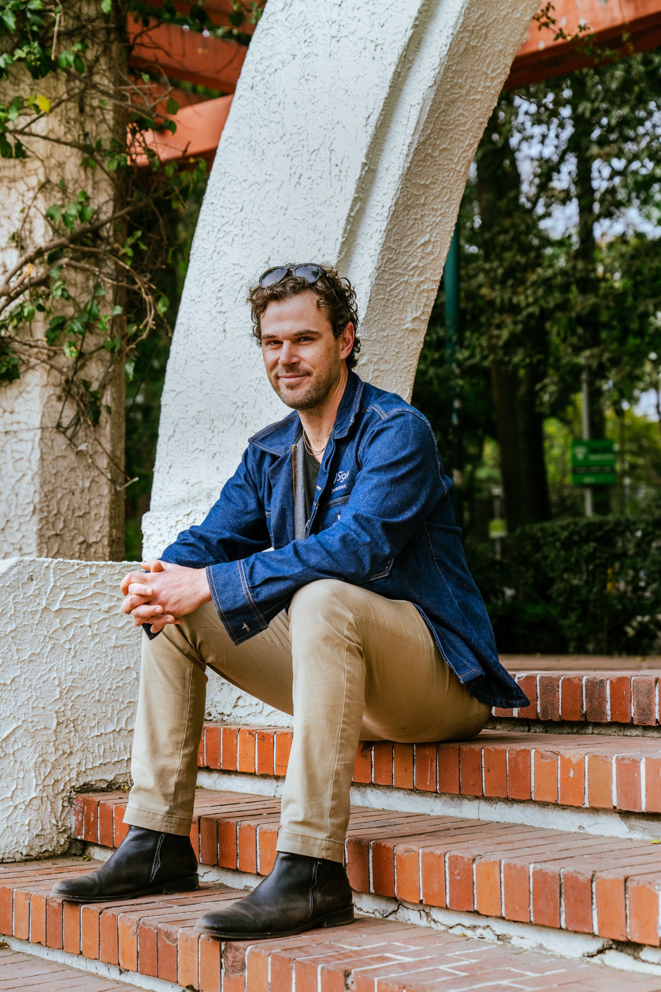 Isaac Phillips, founder of telecoms company Siglo, sitting on brick steps wearing a blue denim shirt and khaki pants