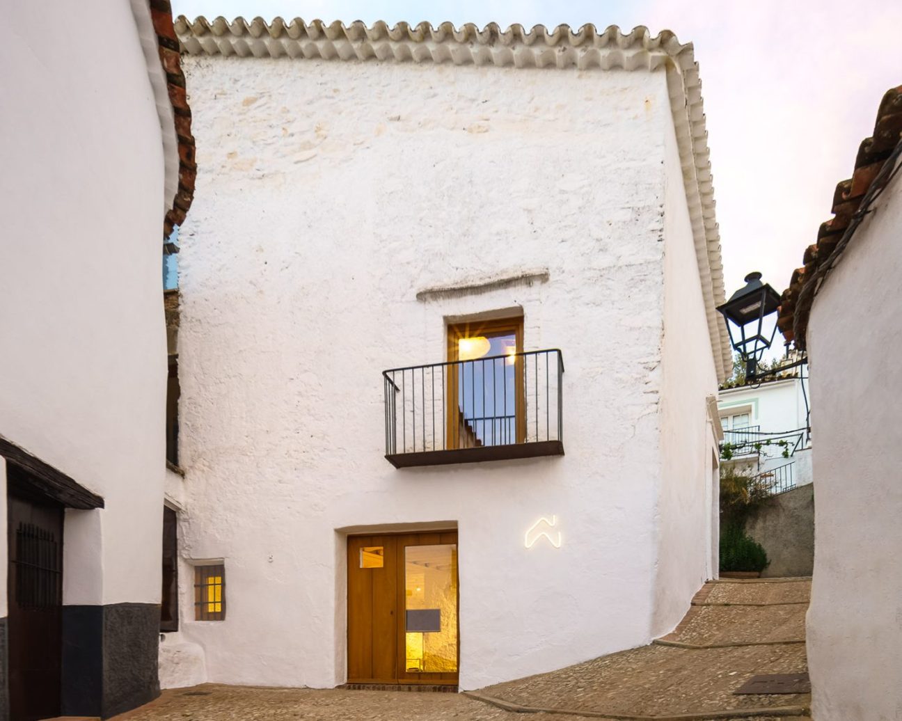 White-washed Mediterranean building with wooden door and balcony on cobblestone street at dusk