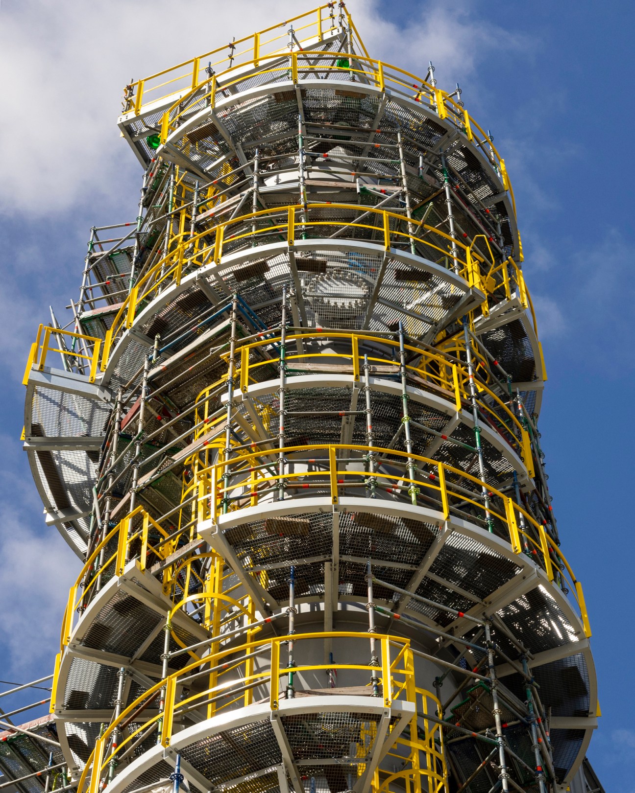 Tall industrial tower with yellow safety railings and metal platforms rising into cloudy sky