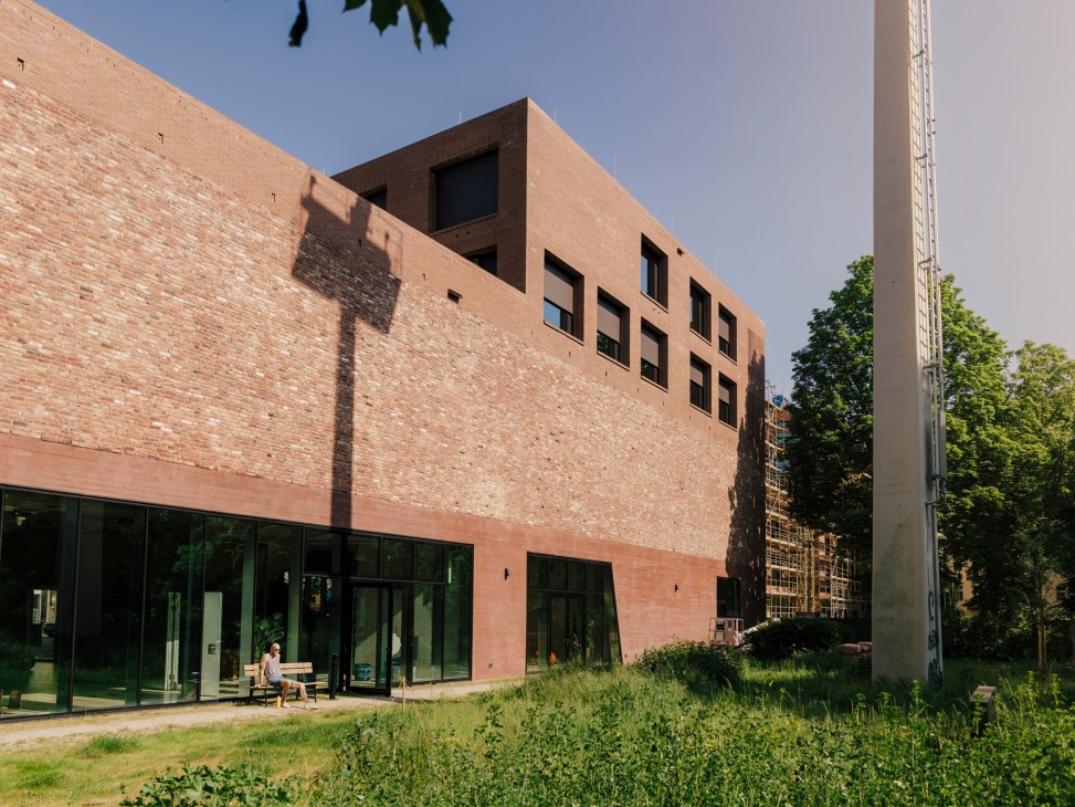 Person sitting on outdoor steps at modern brick building with glass facades and green vegetation