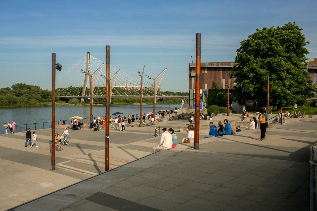 A waterfront public space in Warsaw with people relaxing on concrete steps near the Vistula river