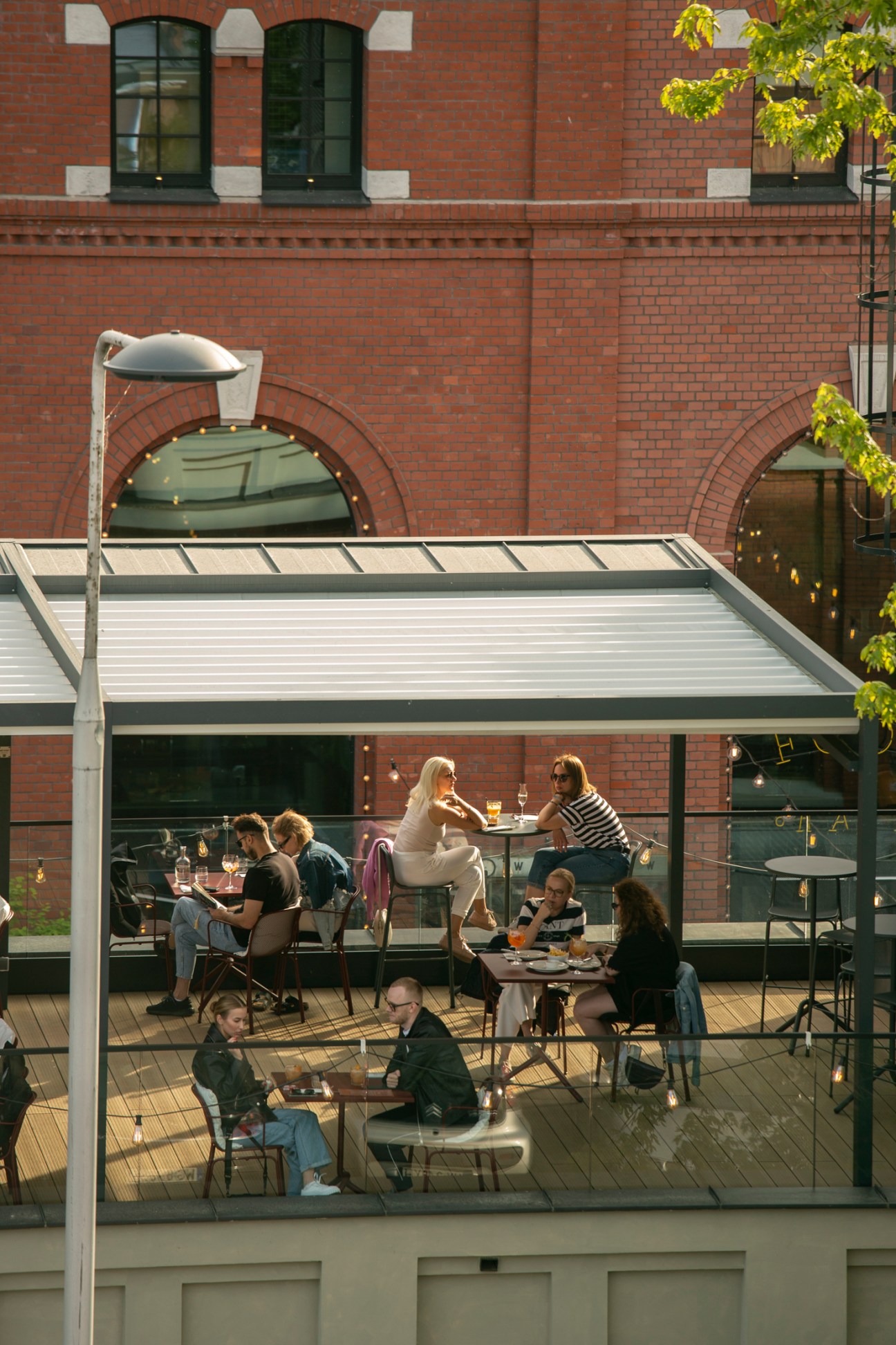 People dining at outdoor restaurant tables under a covered terrace with brick buildings in the background