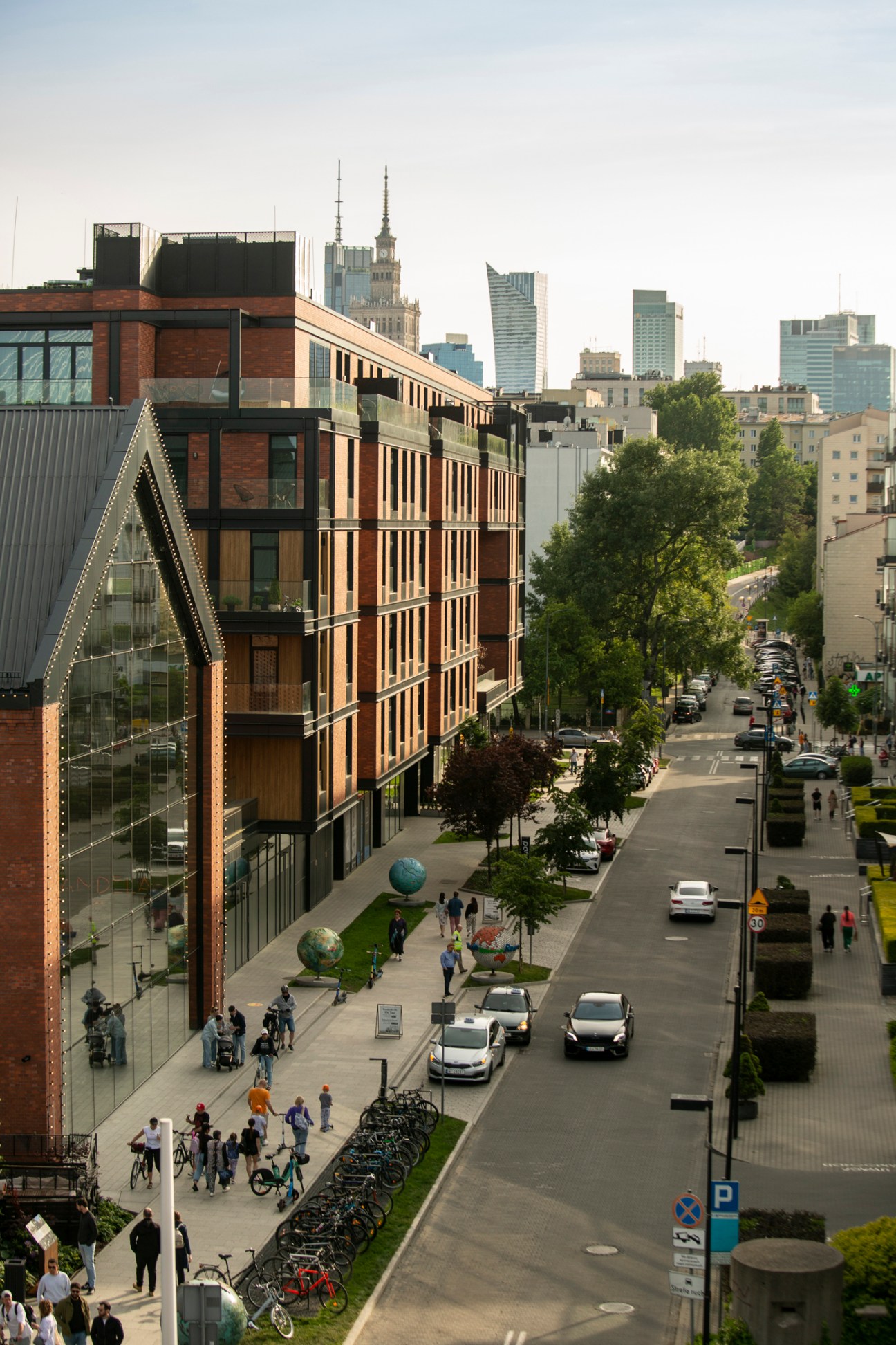 Modern Warsaw street with mixed-use buildings, pedestrians, cars, and bikes lined along the sidewalk