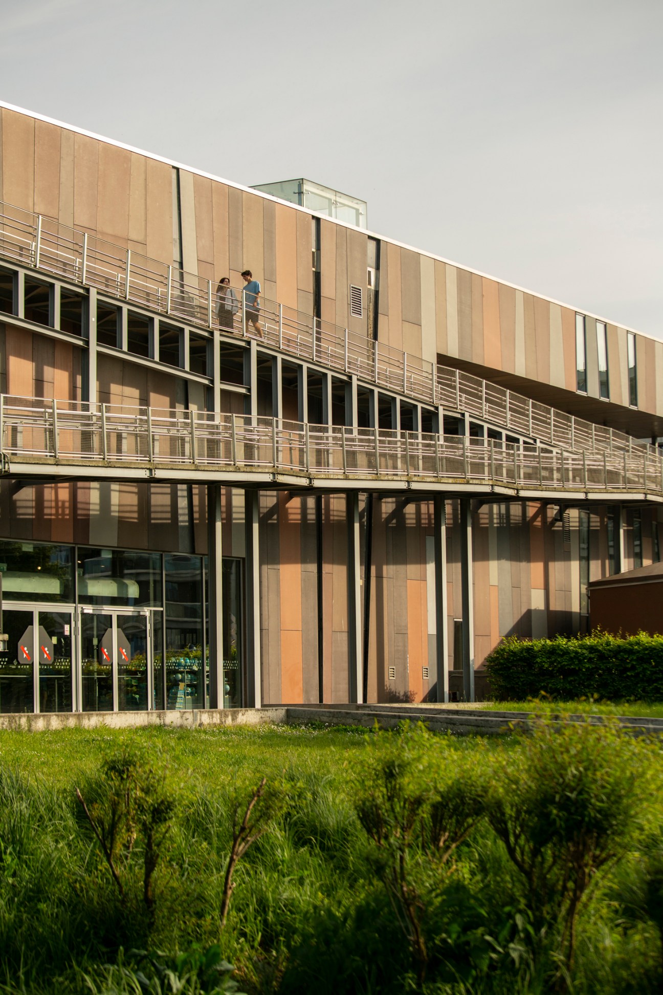 Modern Warsaw building with wooden cladding, horizontal railings, and people walking on exterior walkways