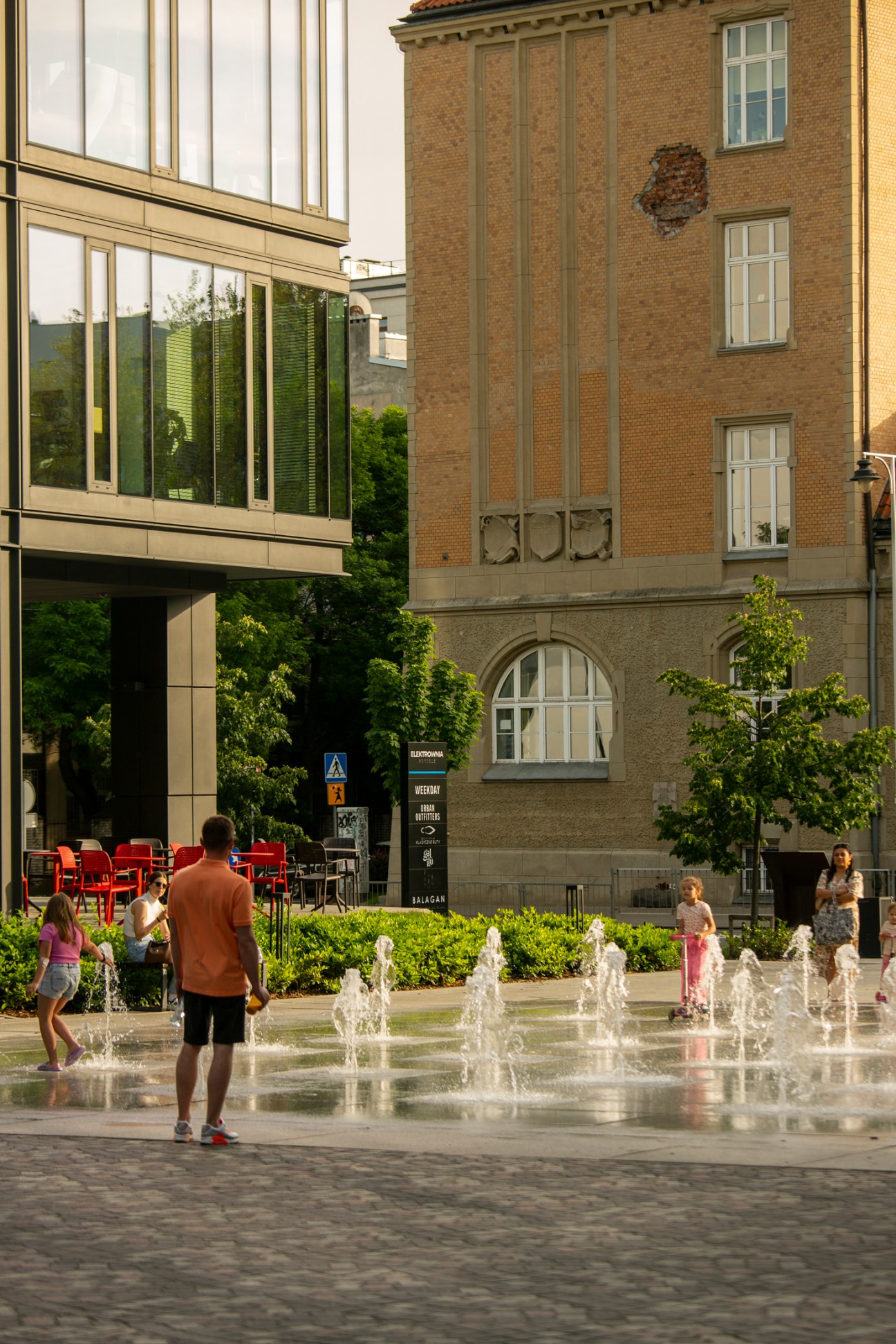 A modern Warsaw plaza with water fountains where families and children play on a sunny day
