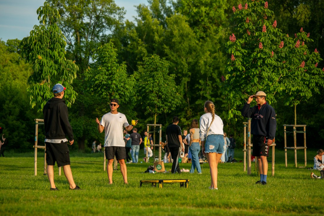 People playing spikeball in a Warsaw park with exercise equipment and lush green trees in the background