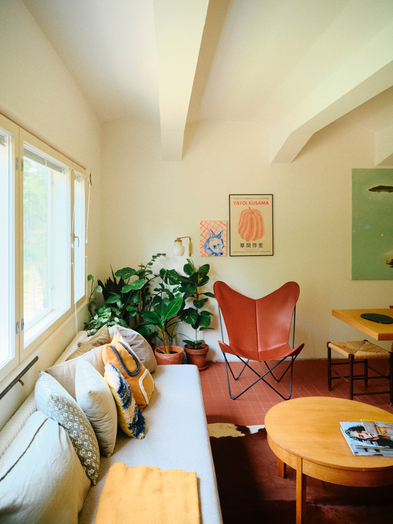 Bright living room with white sofa, orange butterfly chair, plants, and Yayoi Kusama poster on cream walls