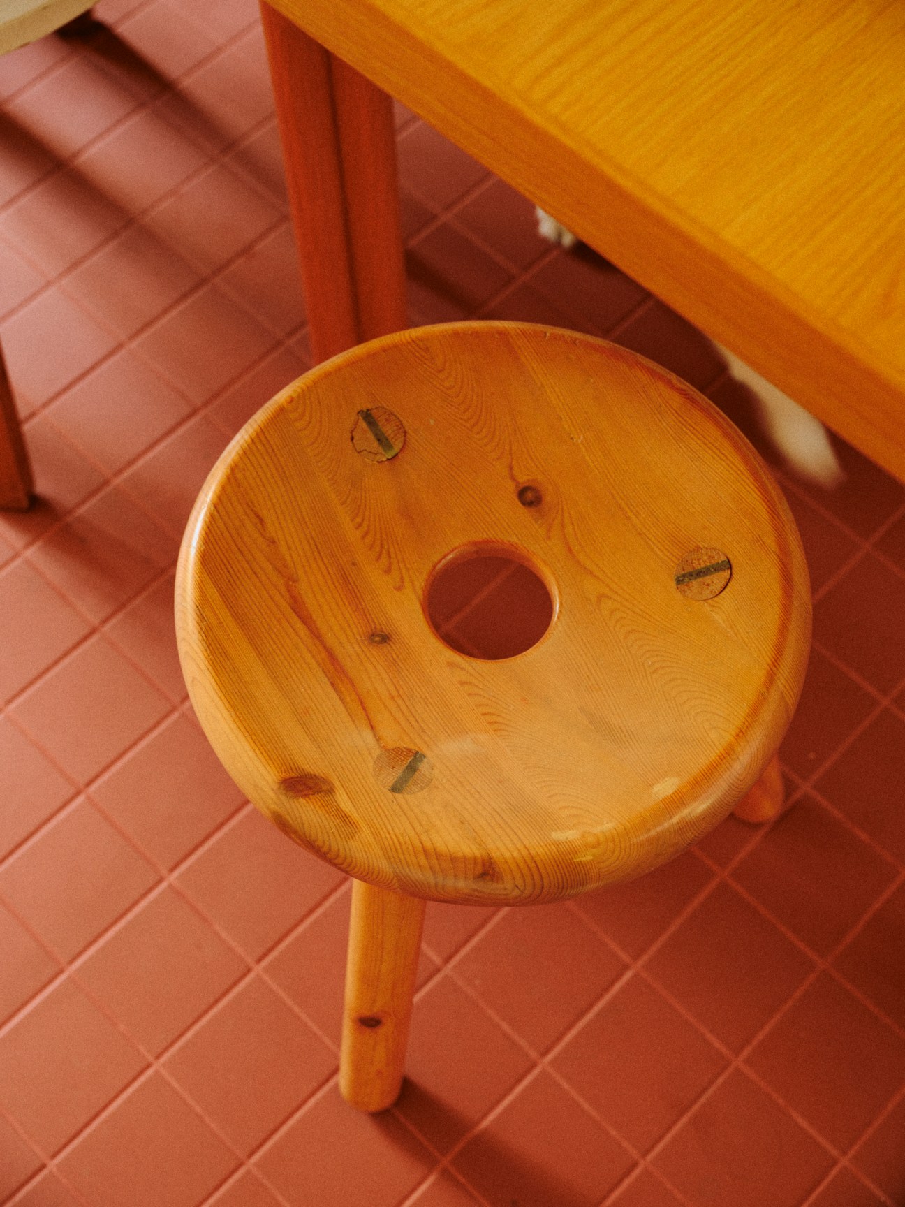 Round wooden pine stool with visible wood grain and knots, featuring a circular hole in the center of the seat
