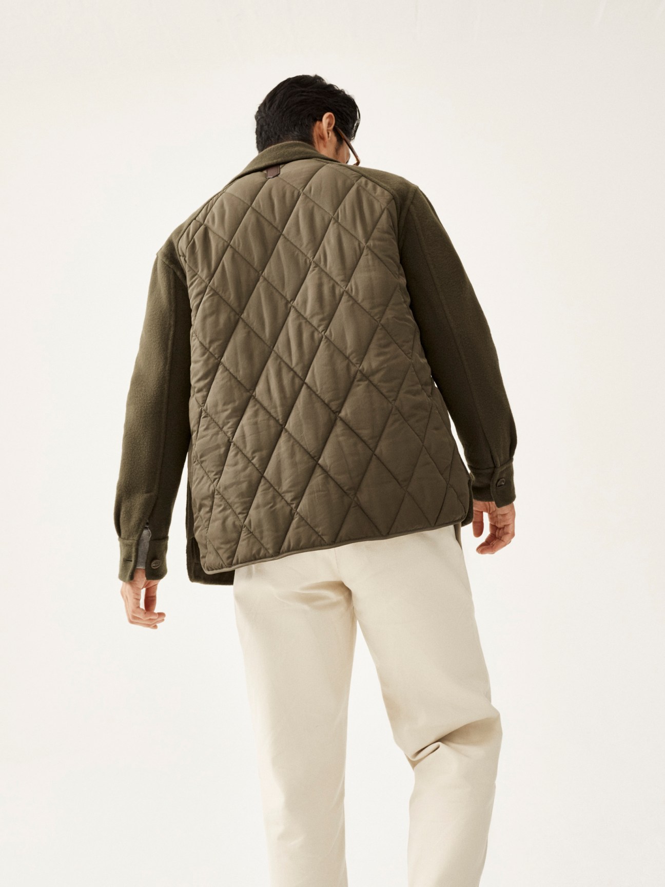 Model wearing olive quilted jacket and cream trousers, shown from behind against white background